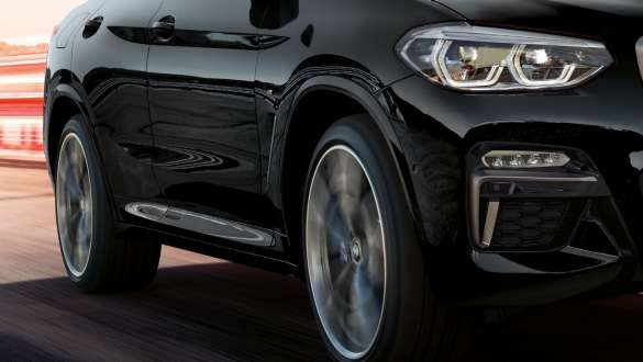 BMW X4 M40i and BMW X4 M40d, three-quarter side view. BMW X4 M40i and BMW X4 M40d in Black Sapphire metallic, driving, exterior, three-quarter side view with rotating light alloy wheels.