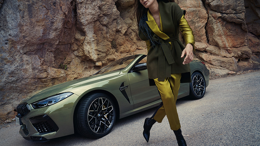 BMW M8 Competition Convertible F91 LCI Facelift 2022 BMW Individual Brass metallic three-quarter front view standing in stony terrain with female model