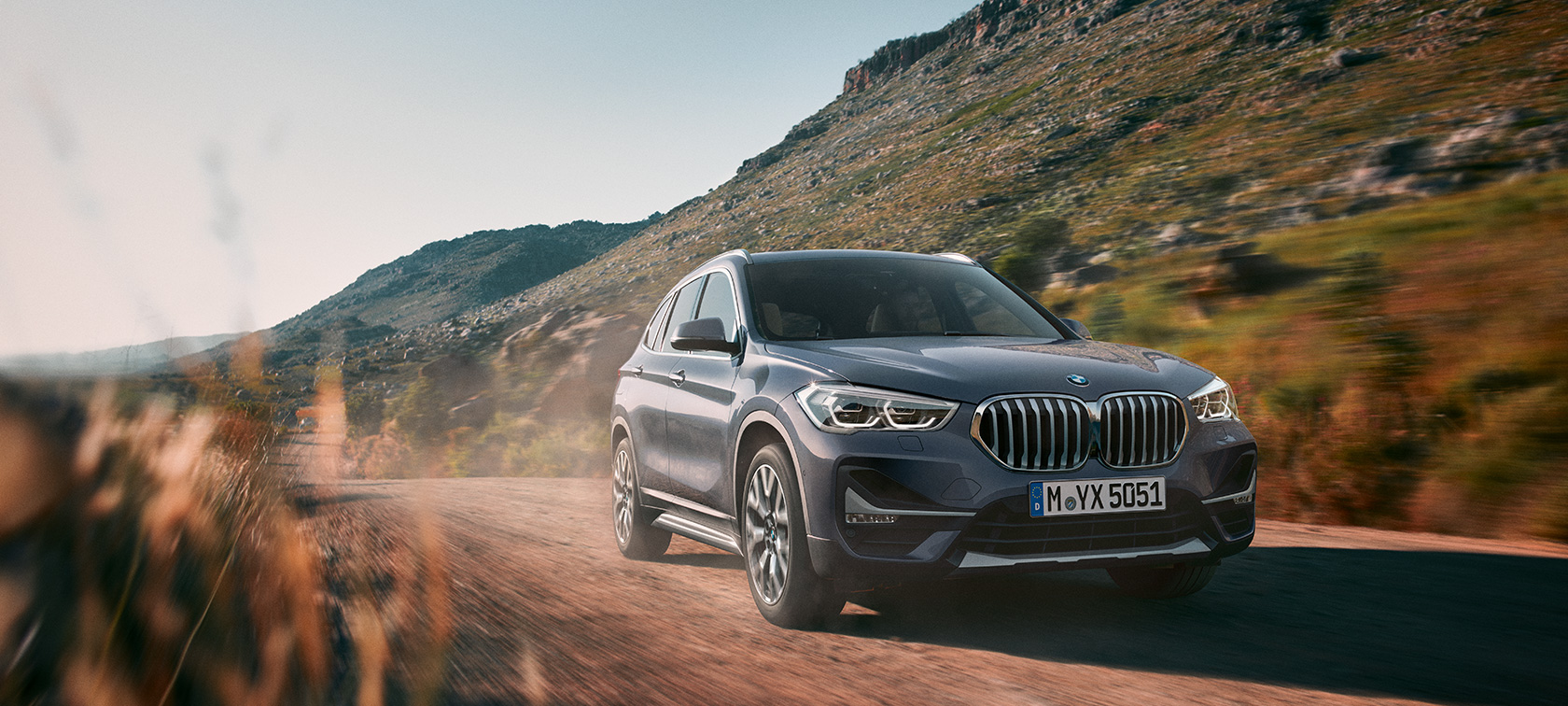 BMW X1, three-quarter front view. BMW X1, three-quarter front view driving in front of mountain scenery.