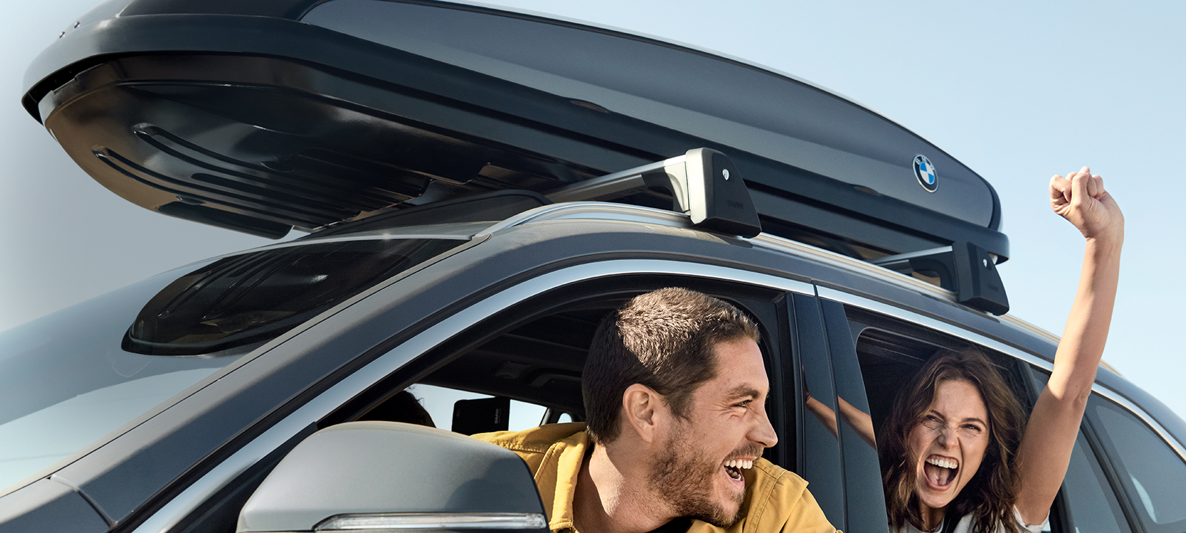 Happy couple in BMW X1 with BMW offers summer Happy couple in BMW X1 Mineral Grey equipped with BMW offers summer three quarter side view under a blue sky