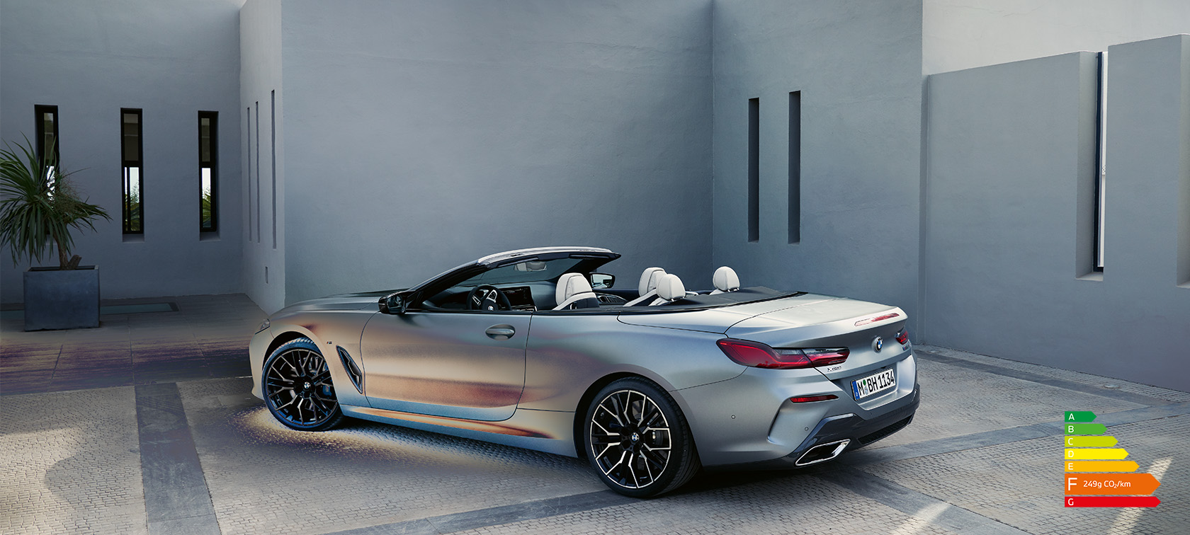 Man leaning against BMW 8 Series Convertible G14 LCI Facelift 2022 BMW Individual Frozen Pure Grey metallic side view standing in front of a building with male model
