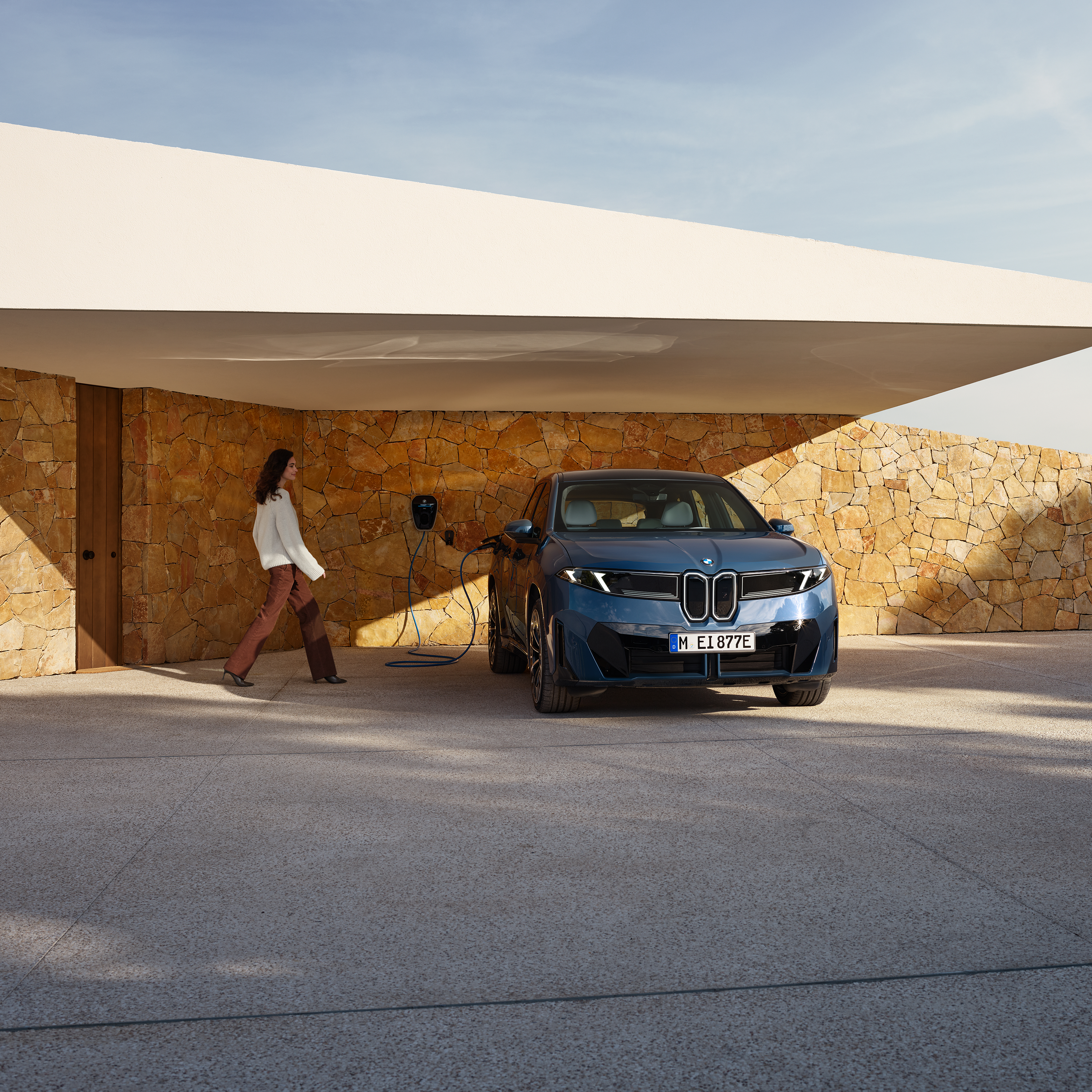 A woman is walking towards a BMW iX3 connected to a wallbox