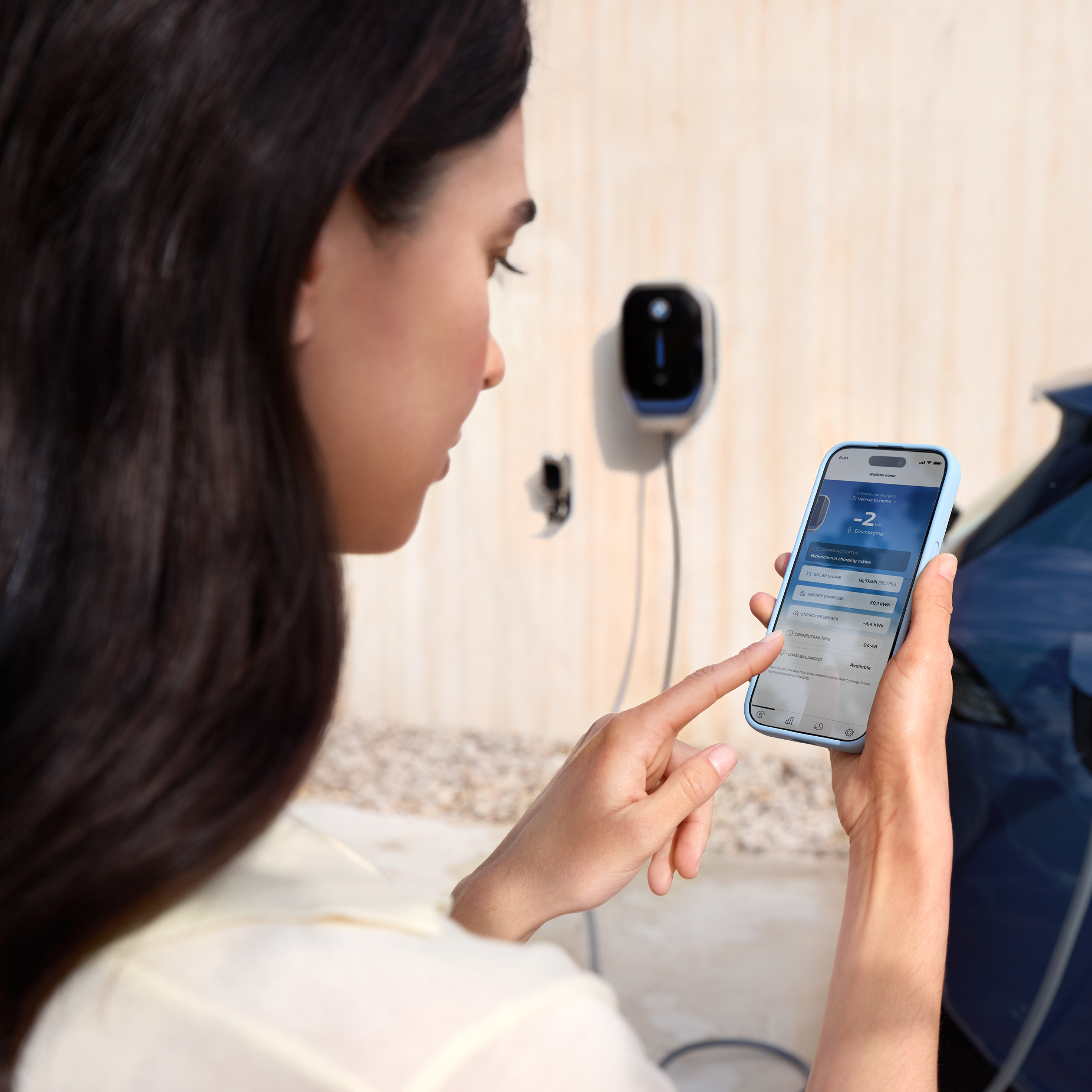 A woman is looking at her smartphone, a wallbox is visible in the background